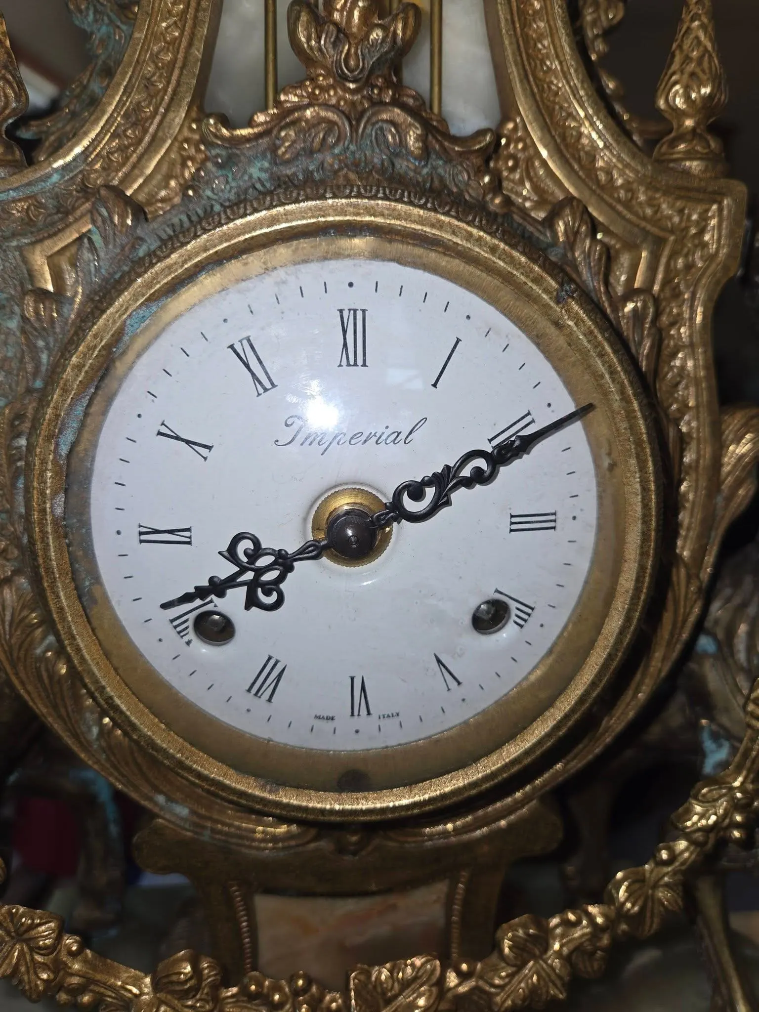 Close-up of an ornate gilt-cased Imperial clock dial with Roman numerals and cast brass floral frame